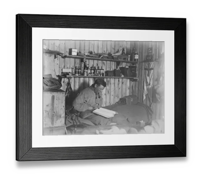 Framed Print : George Murray Levick seated on his bunk, reading